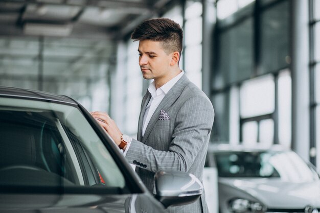 Jonge knappe bedrijfsmens die een auto in een autotoonzaal kiest