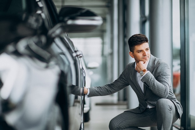 Jonge knappe bedrijfsmens die een auto in een autotoonzaal kiest