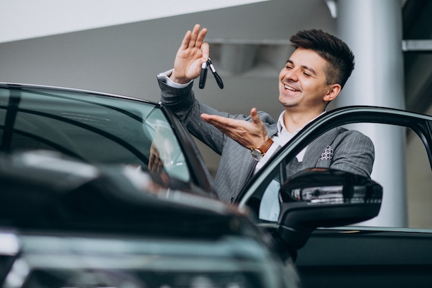 Jonge knappe bedrijfsmens die een auto in een autotoonzaal kiest