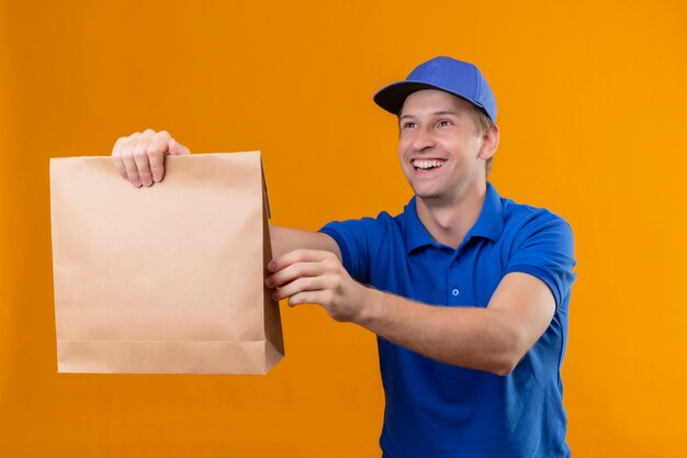 Jonge knappe bezorger in blauw uniform en pet papier pakket geven aan een klant