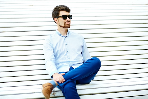 Jonge knappe hipster mannelijke student zittend op de bank in een park