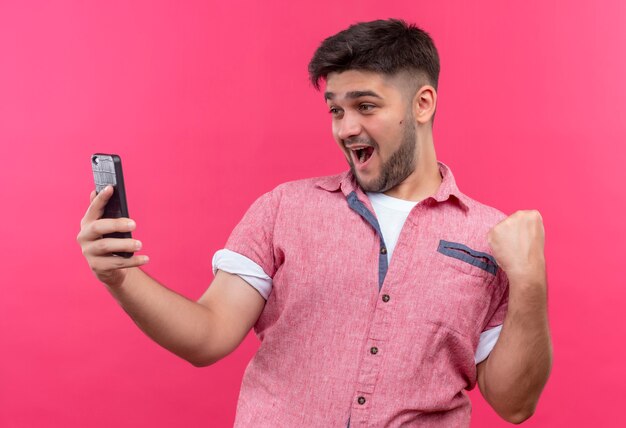 Jonge knappe kerel die roze poloshirt draagt die selfie speels over roze muur maakt