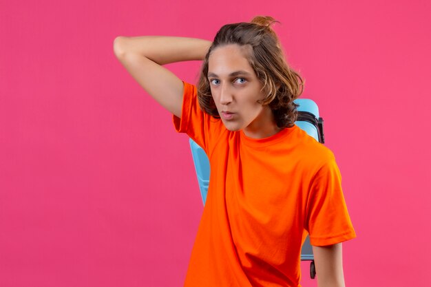 Jonge knappe kerel in oranje t-shirt die zich met reiskoffer bevinden die zeker positief en gelukkig kijken