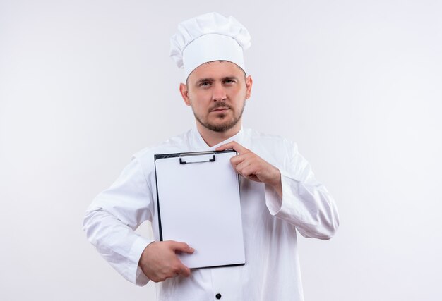 Jonge knappe kok die in het klembord van de chef-kok het eenvormige bedrijf op geïsoleerde witte ruimte kijkt
