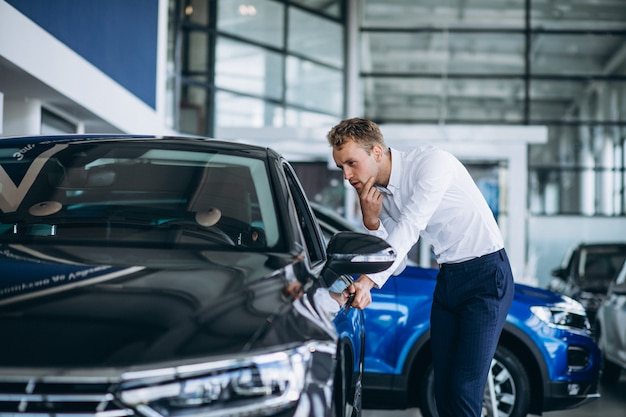 Jonge knappe man die een auto in een autotoonzaal kiest