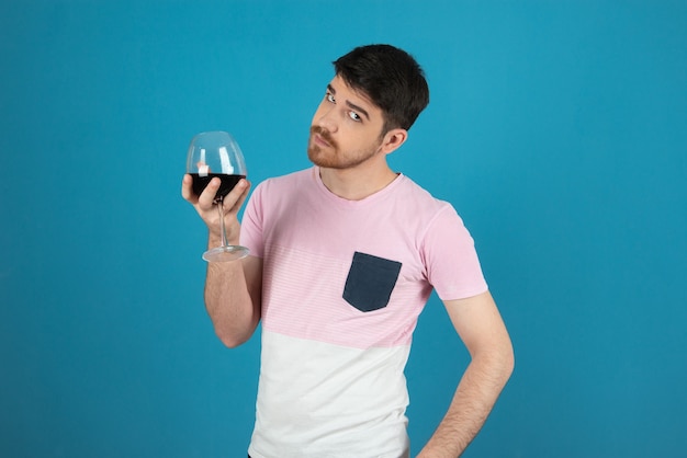 Jonge knappe man die een glas wijn vasthoudt en naar de camera kijkt.