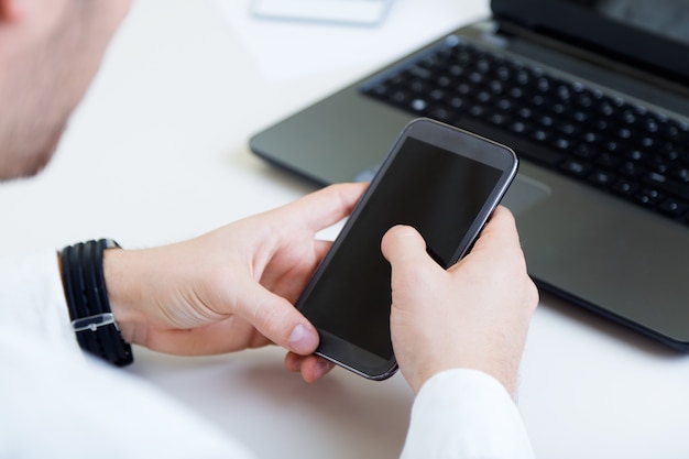 Jonge knappe man die in zijn kantoor met mobiele telefoon werkt.