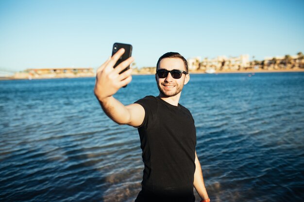 Jonge knappe man doet een zelfportret met smartphone op het strand