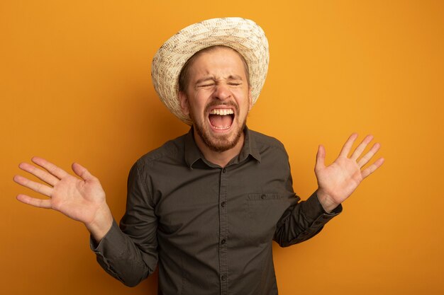 Gratis foto jonge knappe man in grijs shirt en zomerhoed schreeuwen gefrustreerd met opgeheven armen