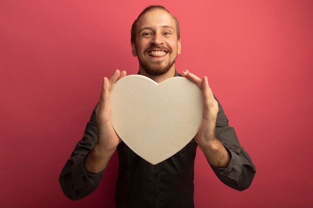 Jonge knappe man in grijs shirt met kartonnen hart met grote glimlach op gezicht