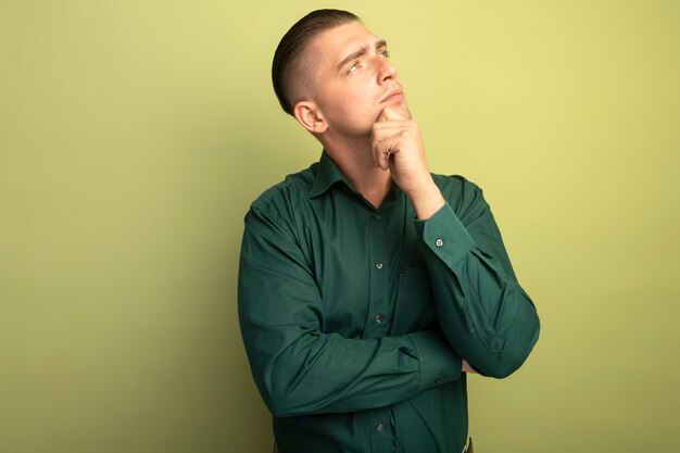 Jonge knappe man in groen shirt opzij kijken verbaasd met hand op kin