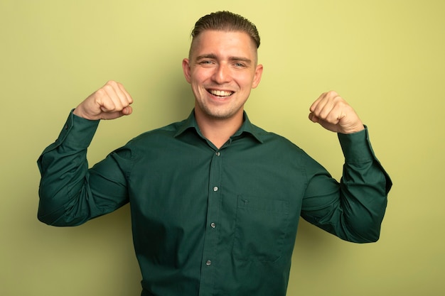 Gratis foto jonge knappe man in groen shirt vuisten gelukkig en positief glimlachend vrolijk