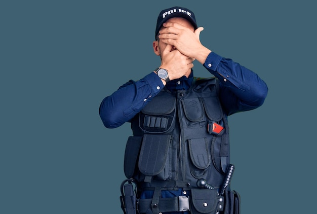 Jonge knappe man in politie-uniform die ogen en mond bedekt met handen verrast en geschokt terwijl hij emotie verbergt