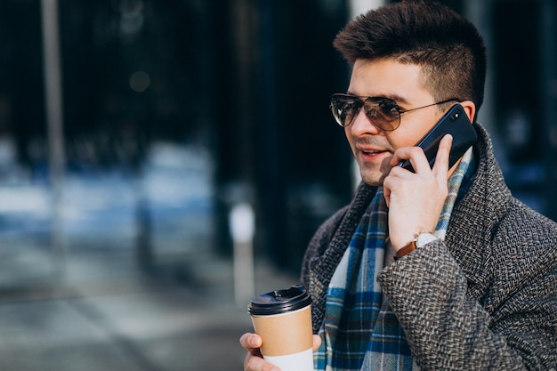 Jonge knappe man koffie buiten drinken en het gebruik van de telefoon