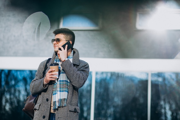 Jonge knappe man koffie buiten drinken en het gebruik van de telefoon