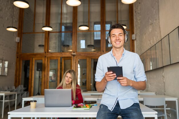 Jonge knappe man met behulp van tablet luisteren naar muziek op draadloze hoofdtelefoons,