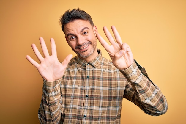 Jonge knappe man met casual shirt die over een geïsoleerde gele achtergrond staat en omhoog wijst met vingers nummer acht terwijl hij zelfverzekerd en gelukkig glimlacht
