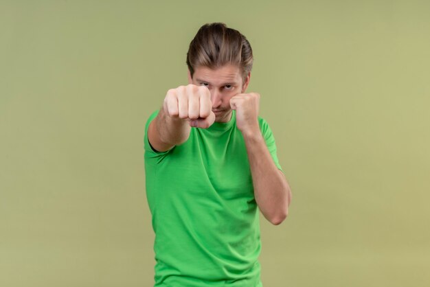 Jonge knappe man met een groen t-shirt die zich voordeed als een bokser met gebalde vuist die zich over groene muur bevindt