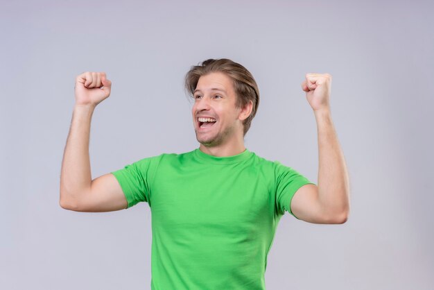 Jonge knappe man met groen t-shirt, opgewonden en blij, gebalde vuisten