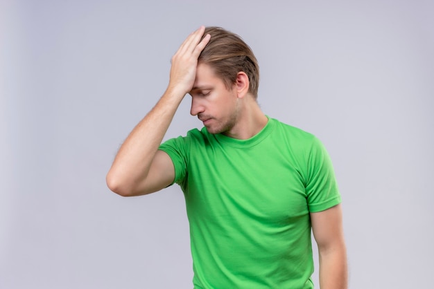 Jonge knappe man met groene t-shirt staande met staande over witte muur