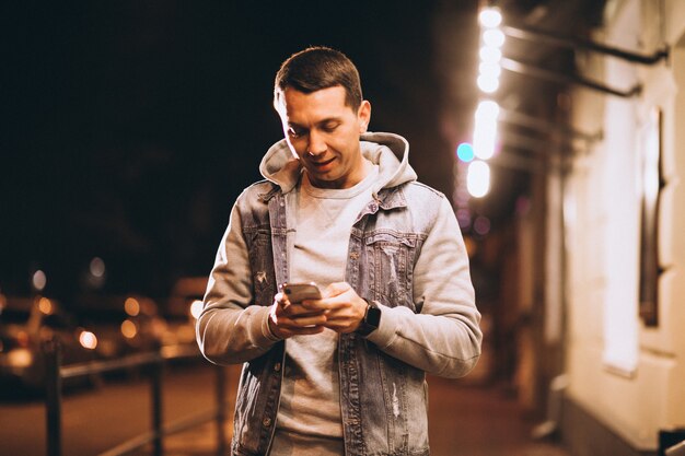 Jonge knappe man met telefoon 's nachts in de straat