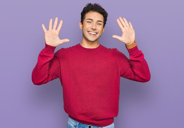 Jonge knappe man met vrijetijdskleding die met vingers nummer tien laat zien en omhoog wijst terwijl hij zelfverzekerd en gelukkig glimlacht.