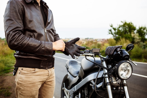 Jonge knappe man poseren in de buurt van zijn motor, het dragen van handschoenen.
