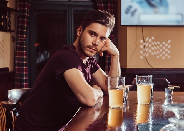 Jonge knappe man rust in de bar of pub, zittend met een glas bier aan houten aanrecht.