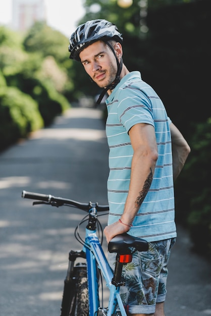 Jonge knappe mannelijke dragende helm die zich met fiets op rechte weg bevinden
