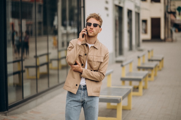 Gratis foto jonge knappe mens die telefoon buiten in de straat met behulp van