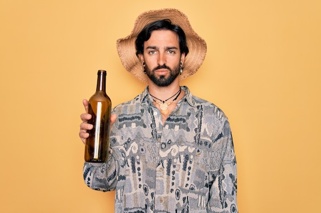 Gratis foto jonge knappe spaanse boheemse hipster man met beer drinkend uit een lege wijnfles met een zelfverzekerde uitdrukking op een slim gezicht serieus denkend