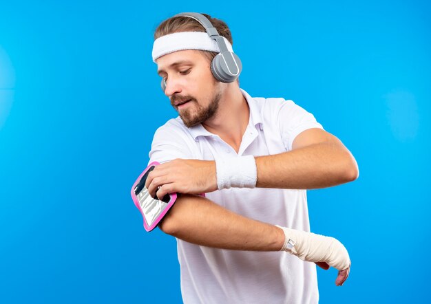 Jonge knappe sportieve man met hoofdband en polsbandjes en koptelefoon met telefoon armband