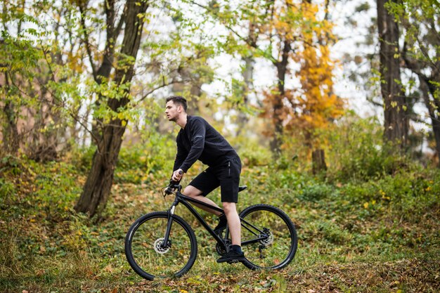 Jonge knappe sportmens met zijn fiets opleiding in park in de herfsttijd.