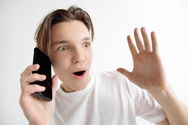 Jonge knappe tiener die het smartphonescherm toont dat op grijze muur wordt geïsoleerd in shock met een verrassingsgezicht