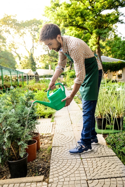 Jonge knappe vrolijke tuinman glimlachen, drenken, planten verzorgen