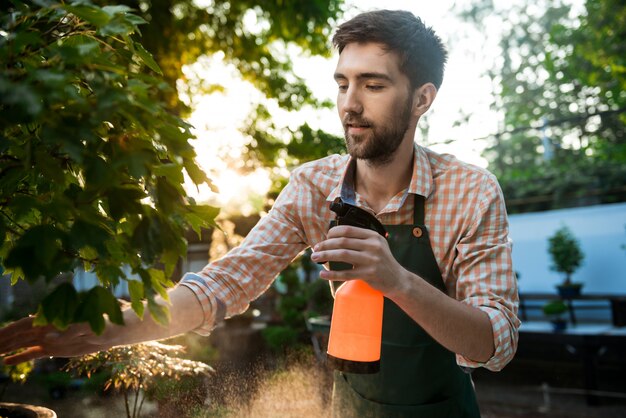 Jonge knappe vrolijke tuinman glimlachen, drenken, planten verzorgen