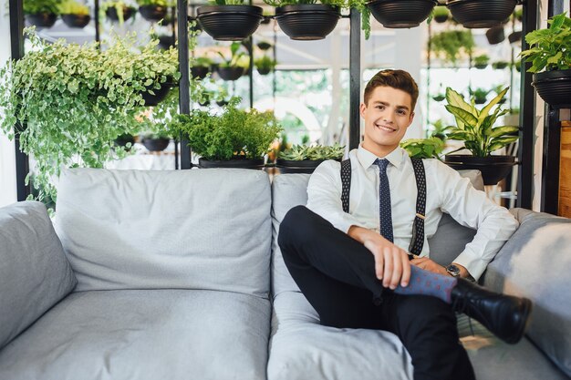 Jonge knappe zakenman zittend in een kantoor op een zomerterras in een wit overhemd met bretels en stropdassen