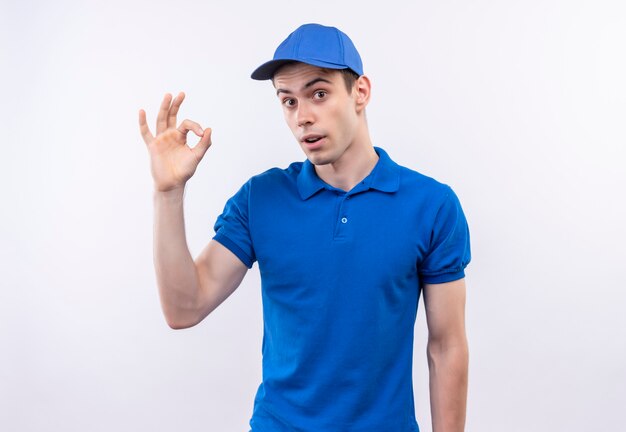 Jonge koerier die blauwe uniform en blauwe pet draagt die ok met vingers doen
