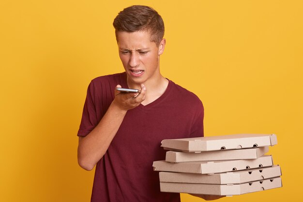 Jonge koerier die onaangenaam gesprek met cliënt telefonisch heeft, die dozen met pizza houdt