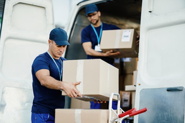 Jonge koerier en zijn collega die kartonnen dozen uit de bestelwagen haalt