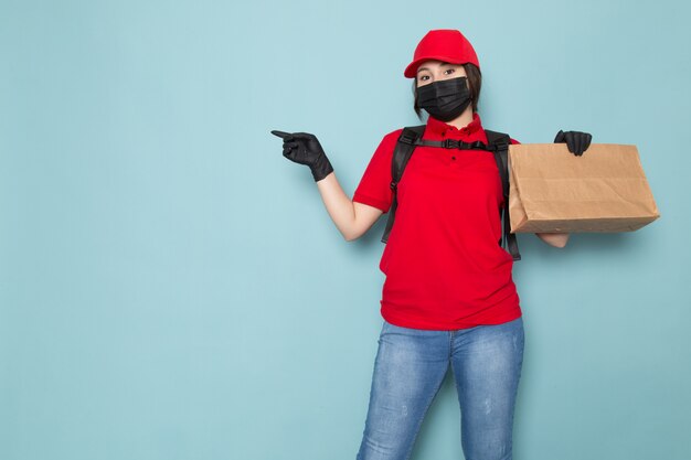 Jonge koerier in rode polo rode dop zwart steriel beschermend masker zwarte rugzak met pakket op blauw