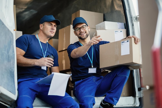 Jonge koerier wijst naar iets terwijl hij samen met zijn collega in de bestelwagen zit