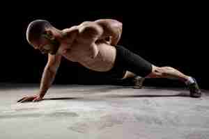 Gratis foto jonge krachtige sportman opleiding push-ups over donkere muur.