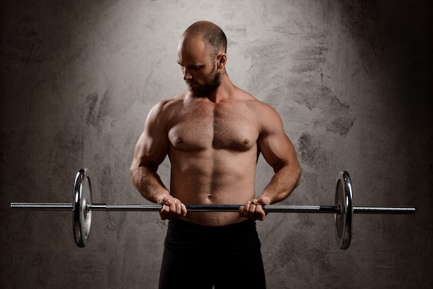 Jonge krachtige sportman training met barbell over donkere muur.