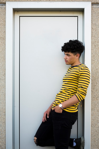 Gratis foto jonge krullende spaanse mens die op deuromhulsel leunt