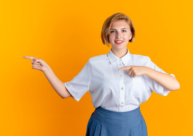 jonge lachende blonde Russische meisje wijst met twee handen aan de zijkant camera kijken