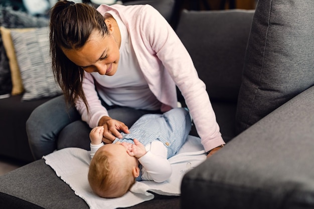 Jonge lachende moeder die voor haar babyjongen zorgt die op de bank ligt