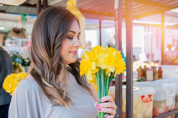 Jonge lachende vrouw kiezen van verse bloemen. Close-up profiel portret van een mooie en jonge vrouw genieten van en ruiken een boeket bloemen terwijl ze staan ​​in een verse bloemenmarkt kraam tijdens een zonnige dag in openlucht.