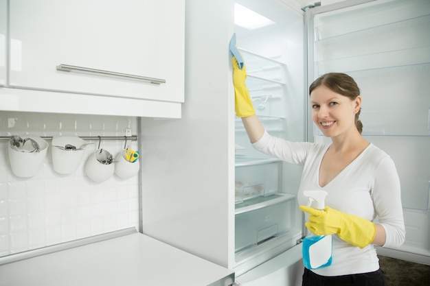 Jonge lachende vrouw met rubberen handschoenen die de koelkast schoonmaken