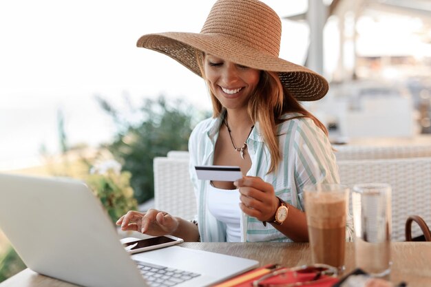 Jonge lachende vrouw ontspannen in een café tijdens het gebruik van mobiele telefoon en creditcard voor online bankieren